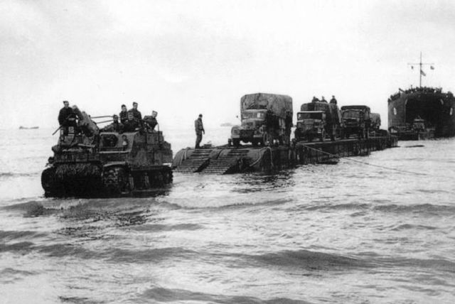 La 1st British Division desembarcando en Peter beach. Un obús autopropulsado Priest 105 mm precede a una columna de camiones