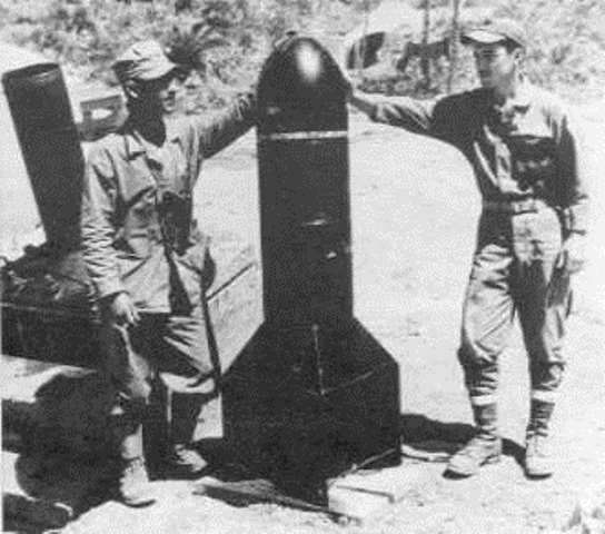 Los marines sostienen un proyectil, detrás de ellos el mortero